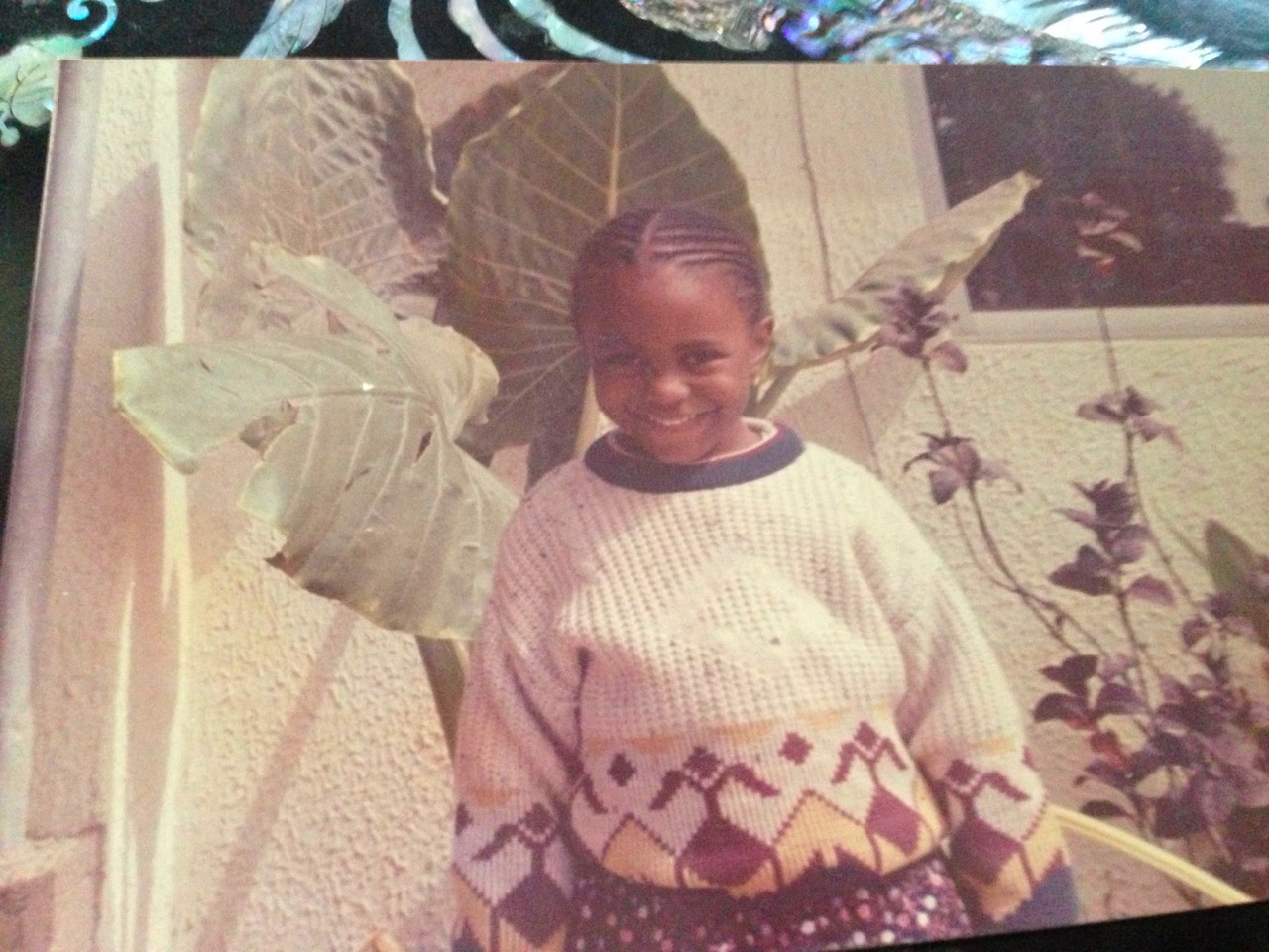 Amal smiling beside leafy plants as a child