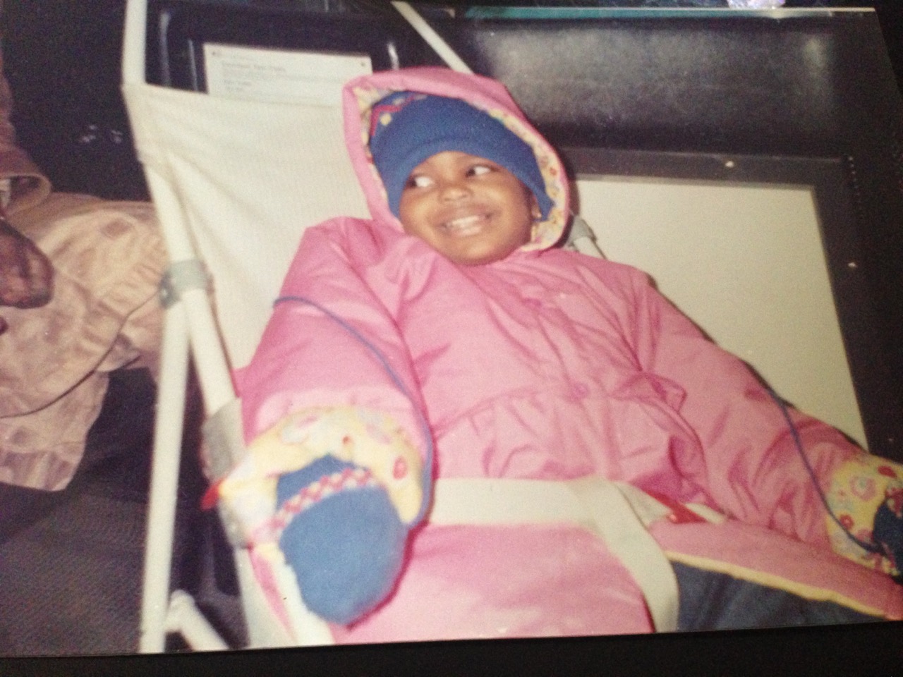 Amal smiling in a pink winter coat as a child