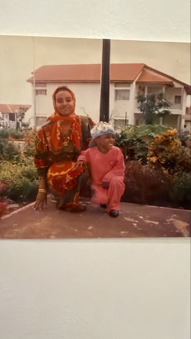 Amal beside a relative in a garden during childhood