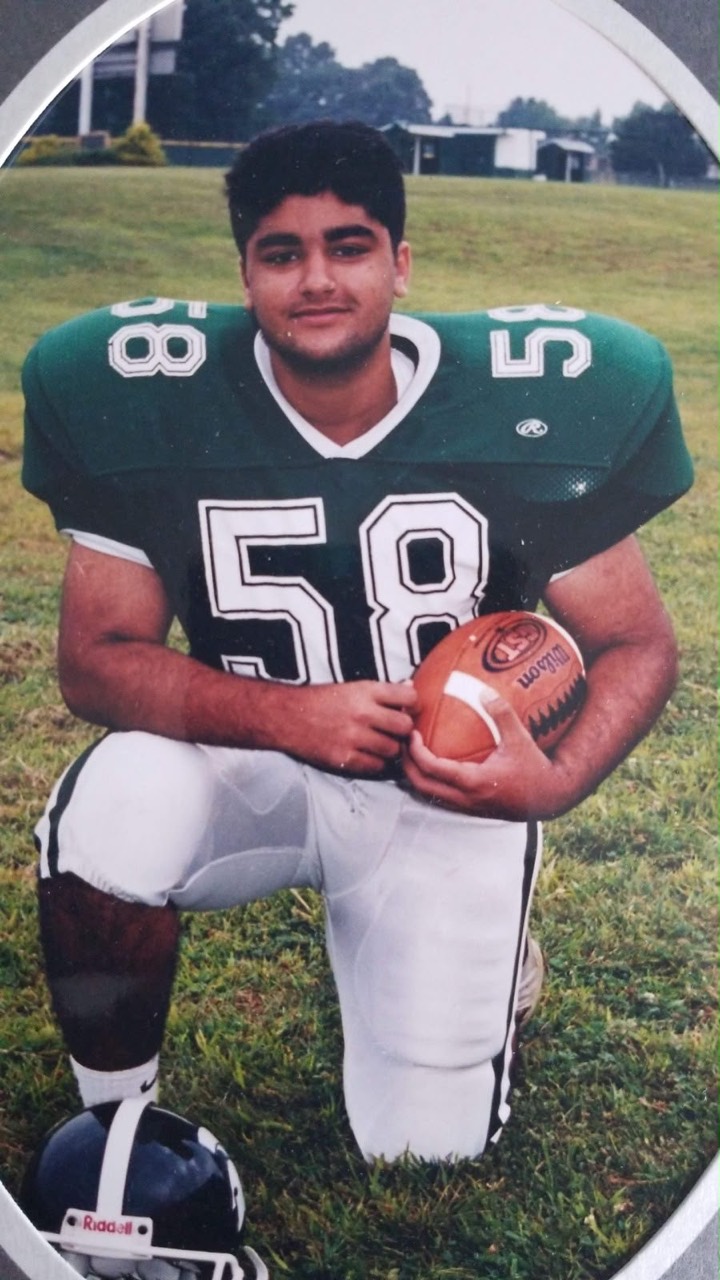 Usman kneeling in a green football uniform and holding a football